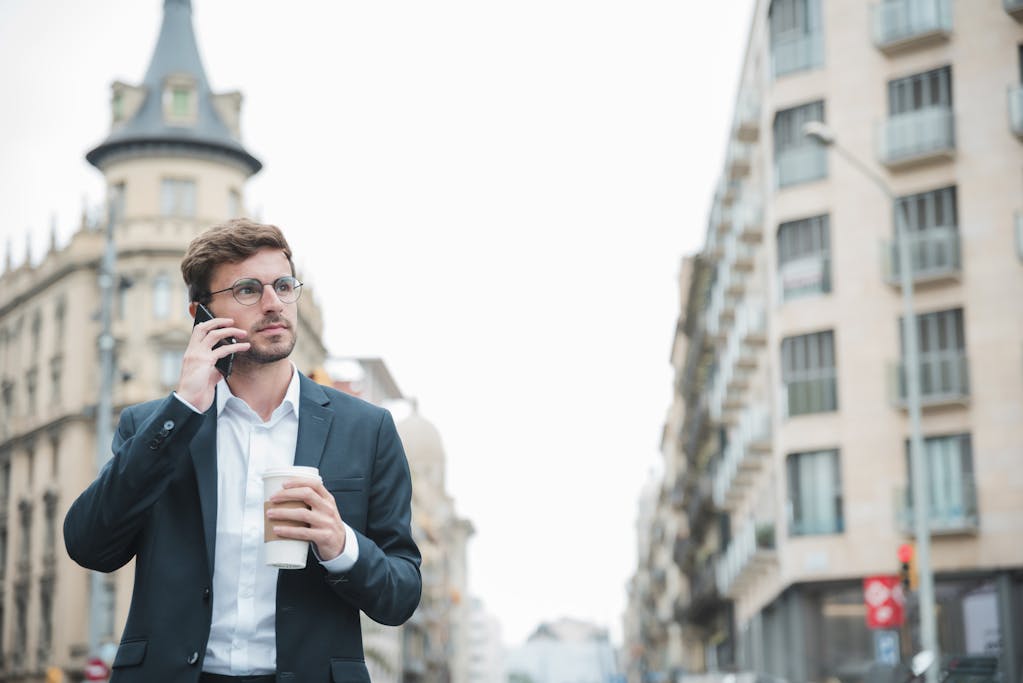Businessman holding standing on street holding takeaway coffee cup in hand talking on mobile phone