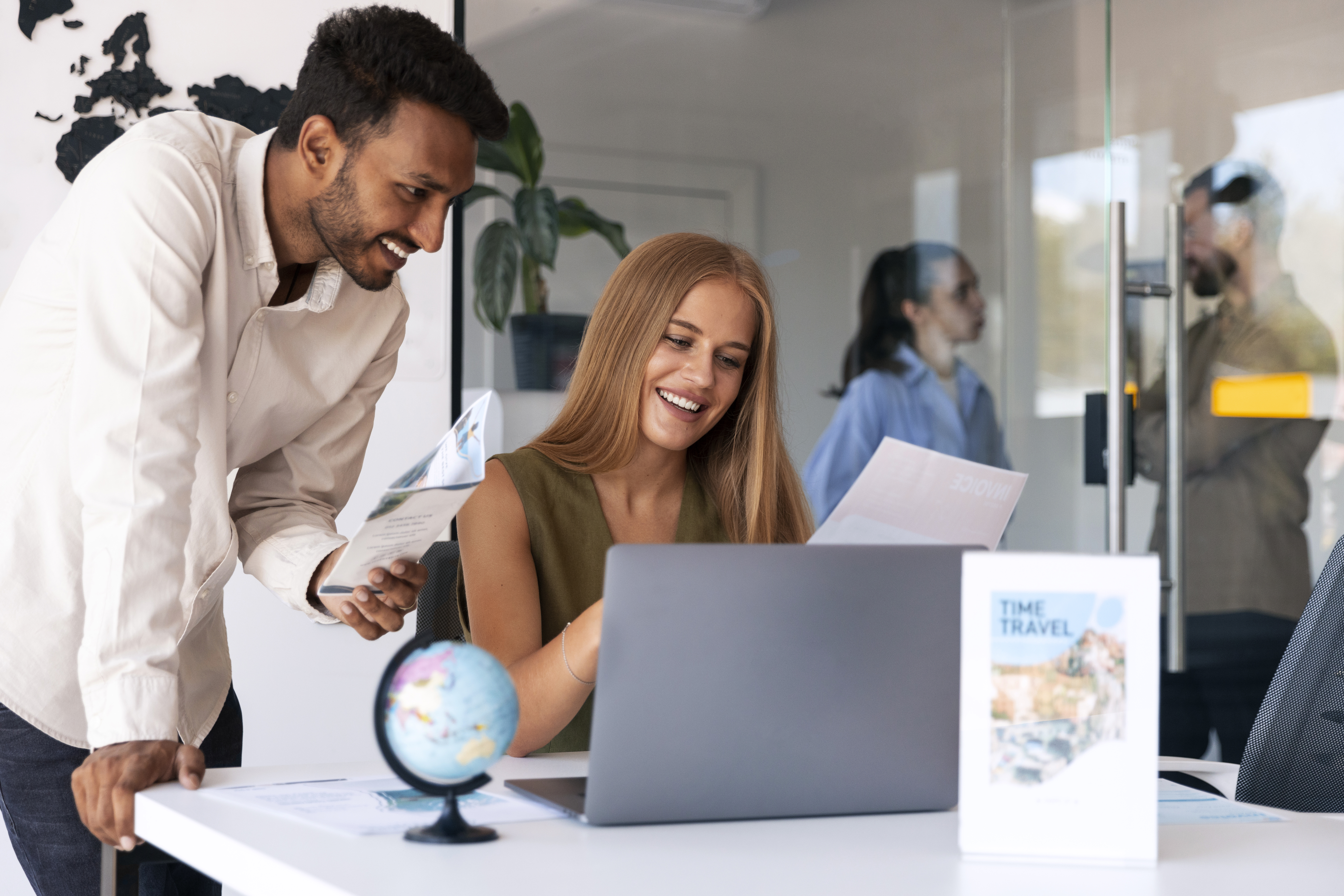 Two young professionals are working together and smiling in their office while looking at information on the computer. 