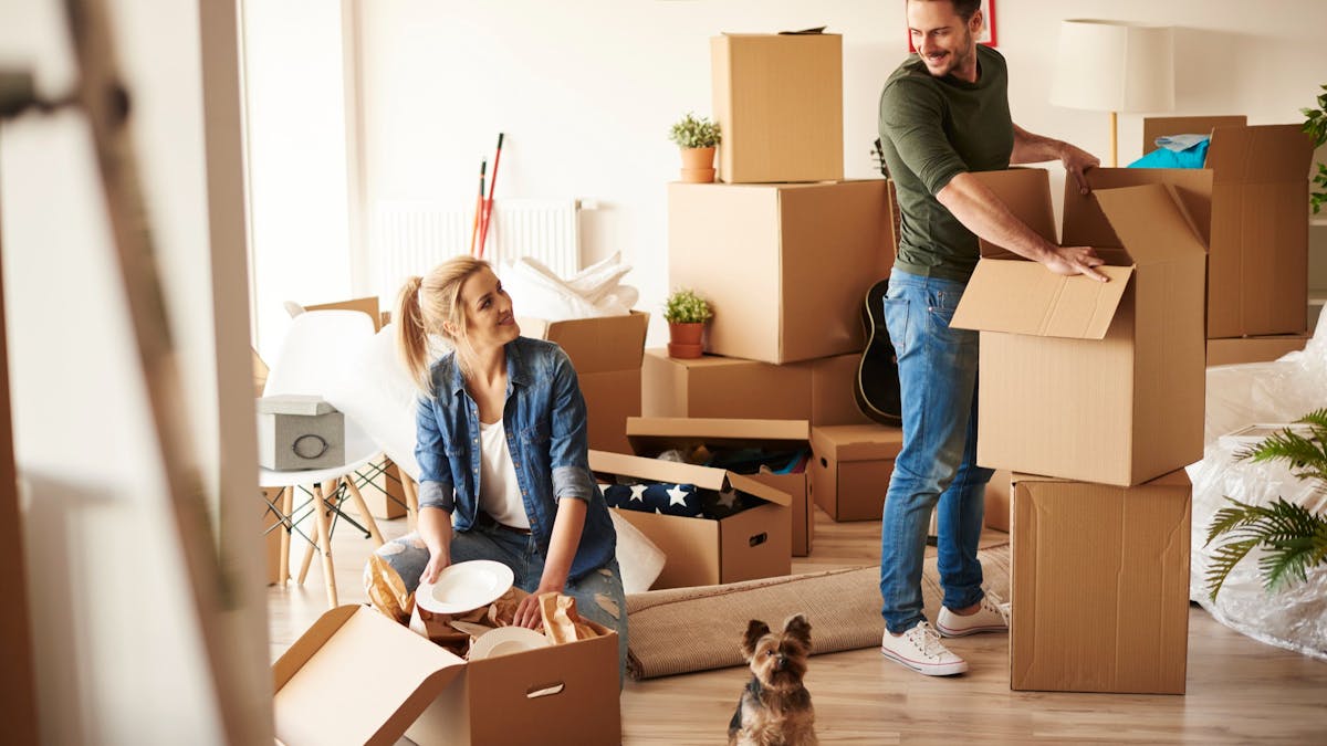 Young couple unpacking boxes in new apartment with small dog