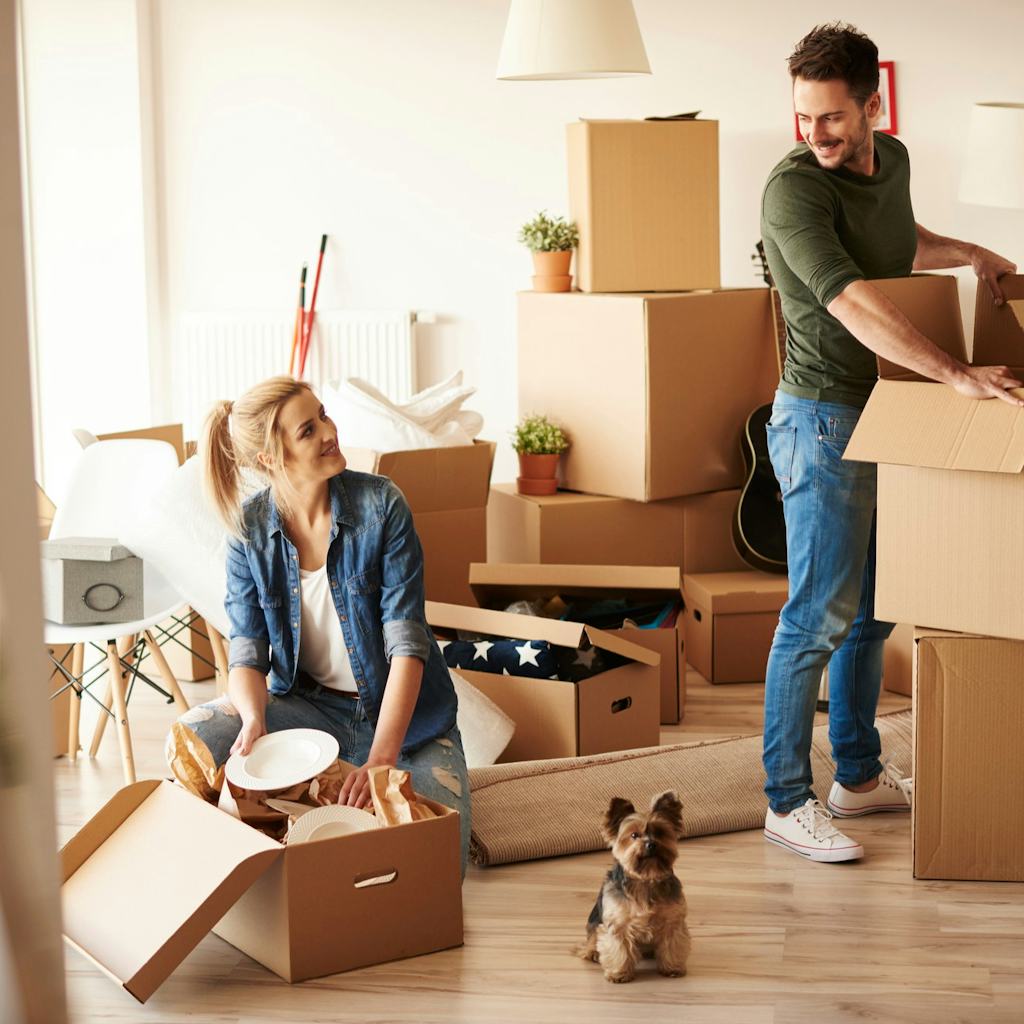 Young couple unpacking boxes in new apartment with small dog