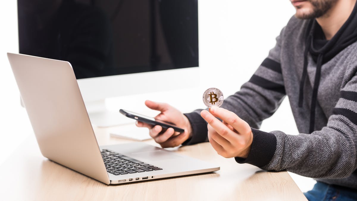 close-up-hands-man-working-place-woth-laptop-monitor-screen-holding-phone-bitcoin