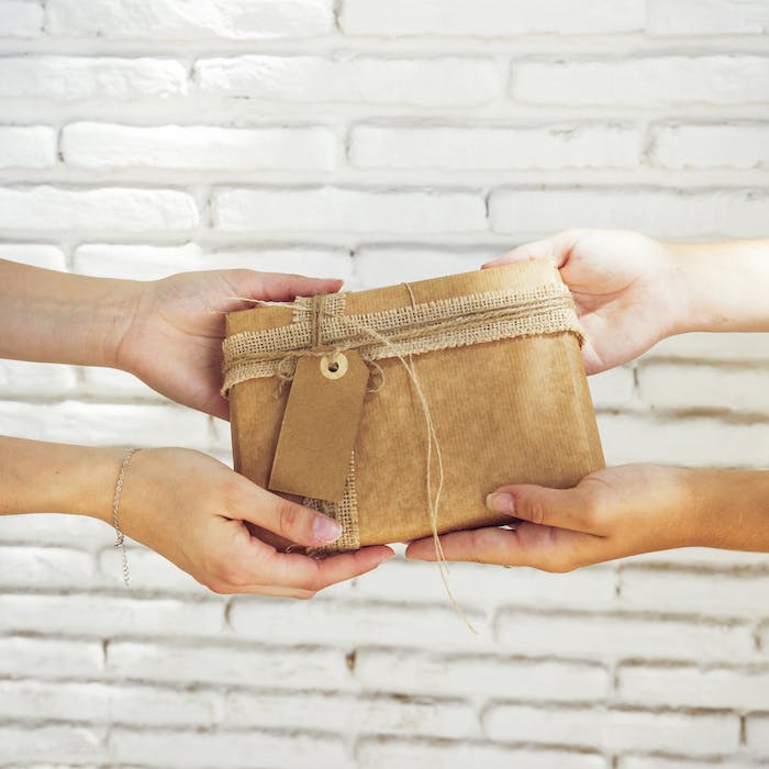 Dos manos sosteniendo un regalo. Imagen por <a href="https://www.freepik.com/free-photo/close-up-two-women-s-hand-holding-birthday-gift_3027244.htm#query=gift%20inheritance&position=36&from_view=search&track=ais">Freepik</a>