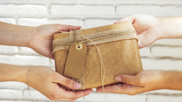 Dos manos sosteniendo un regalo. Imagen por <a href="https://www.freepik.com/free-photo/close-up-two-women-s-hand-holding-birthday-gift_3027244.htm#query=gift%20inheritance&position=36&from_view=search&track=ais">Freepik</a>