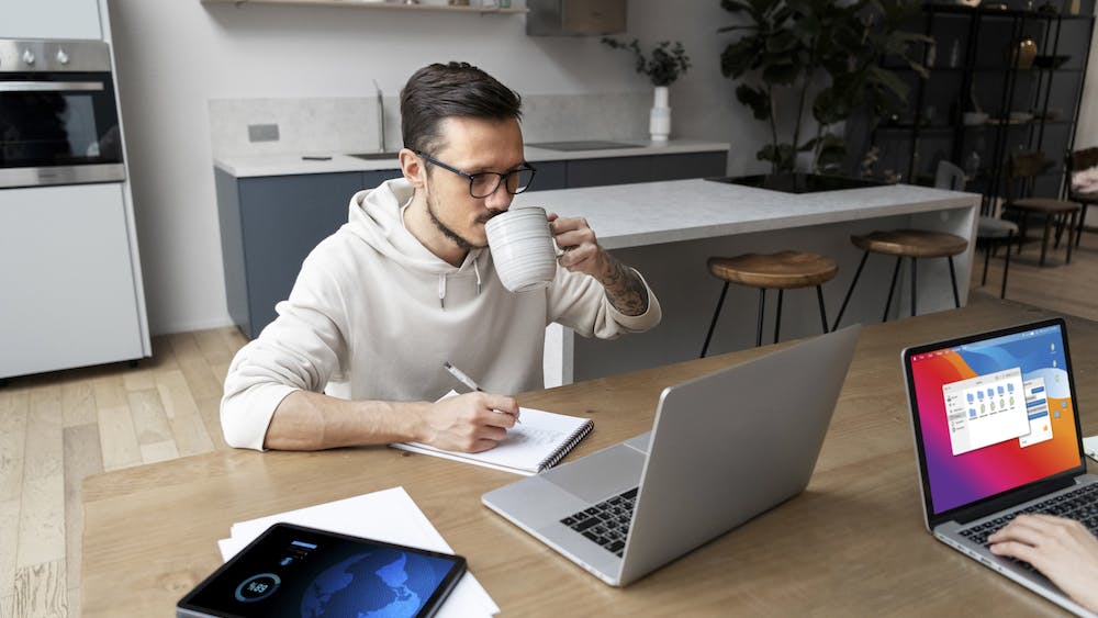 Photo of a man working from home at desk while having a coffee. Image by <a href="https://www.freepik.com/free-photo/man-working-from-home-desk-while-having-drink_21076515.htm#page=2&query=remote%20worker&position=19&from_view=search&track=ais">Freepik</a>
