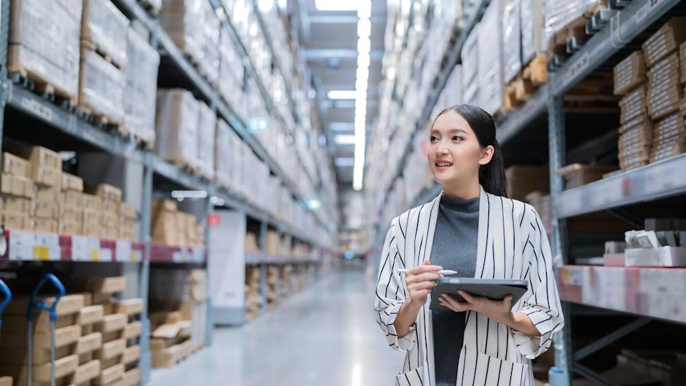 Retrato de una mujer asiática propietaria de un negocio utilizando una tableta digital para comprobar la cantidad de productos en stock en las estanterías de un almacén. <a href="https://www.freepik.com/free-photo/portrait-asian-woman-business-owner-using-digital-tablet-checking-amount-stock-product-inventory-shelf-distribution-warehouse-factorylogistic-business-shipping-delivery-service_25192338.htm#query=business%20export%20owner&position=32&from_view=search&track=ais">Image by Lifestylememory</a> on Freepik