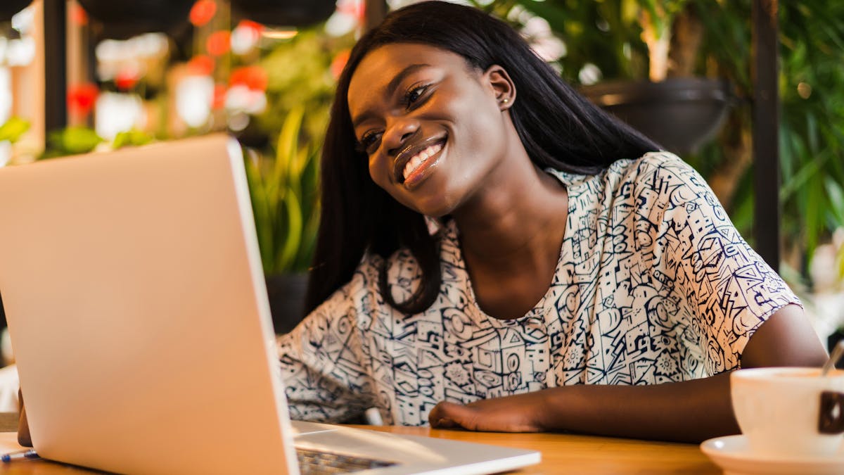 Young african woman siting at cafe smiling and working on laptop <a href="https://www.freepik.com/photos/coffee">Coffee photo created by diana.grytsku - www.freepik.com</a>