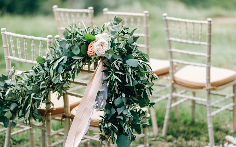 Sillas en un jardín con arreglos florales sobre ellas por motivo de celebración de boda