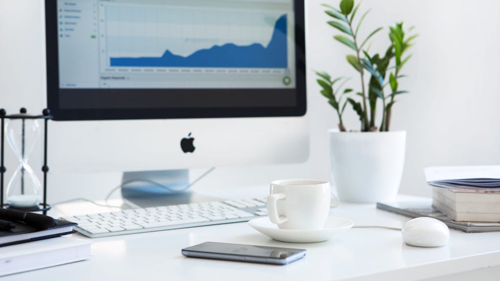 Desktop with keyboard, monitor, teacup, plant and hourglass