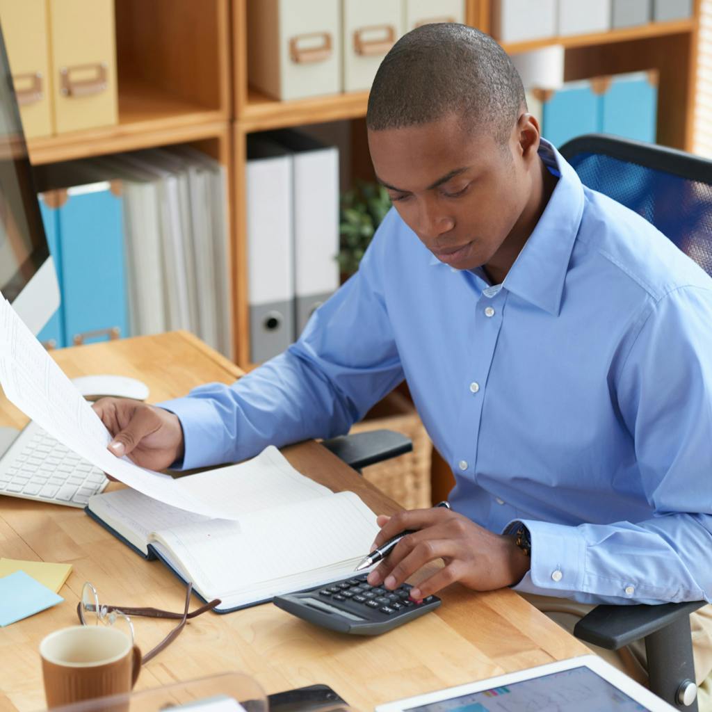 Man with blue collar shirt using a calculator with a sheet of paper in right hand