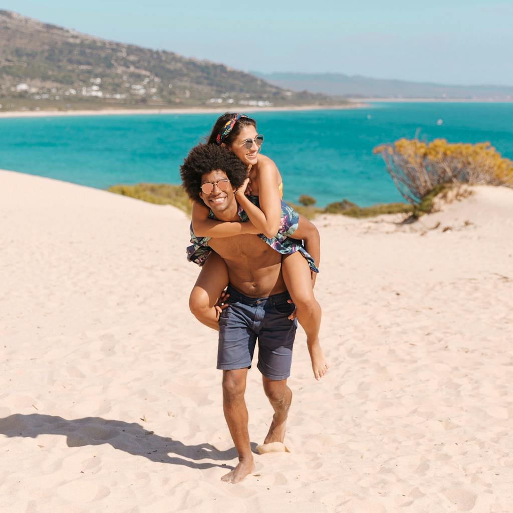 Young man carrying young woman on his back as they enjoy the beach
