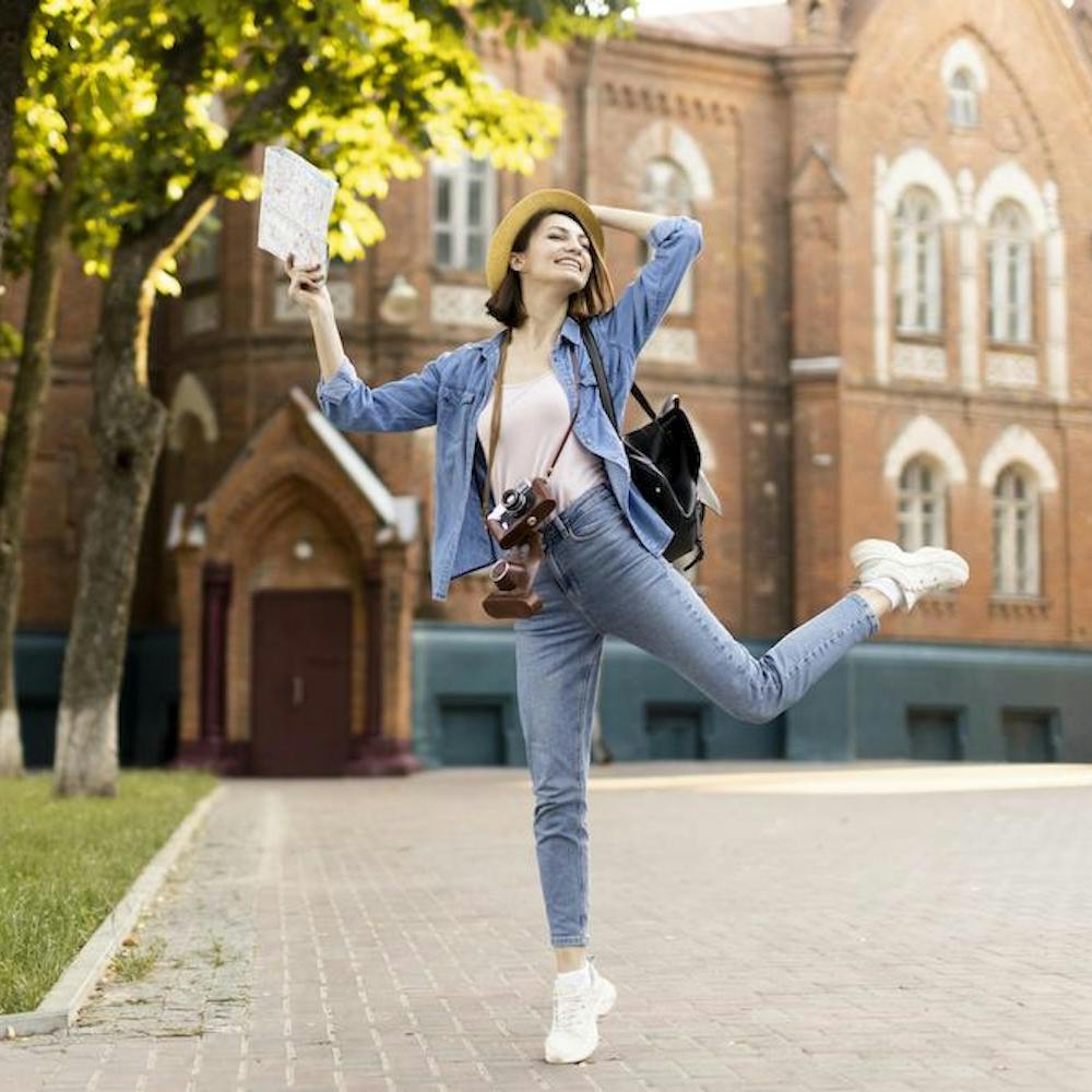 Young female stundent traveller enjoying holidays in front of a historical university building. Image by <a href="https://www.freepik.com/free-photo/young-traveller-enjoying-holidays_9129390.htm#query=free%20student&position=45&from_view=search&track=ais">Freepik</a>