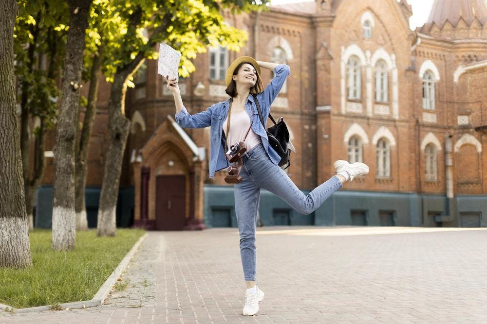 Young female stundent traveller enjoying holidays in front of a historical university building. Image by <a href="https://www.freepik.com/free-photo/young-traveller-enjoying-holidays_9129390.htm#query=free%20student&position=45&from_view=search&track=ais">Freepik</a>