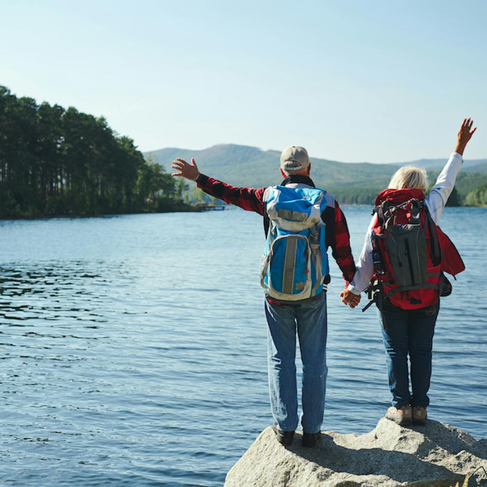 Summer adventure . Couple standing in front of a lake while holding hands and raising the arms up in the air while enjoying the view.<a href='https://www.freepik.com/photos/pension'>Pension photo created by pressfoto - www.freepik.com</a>