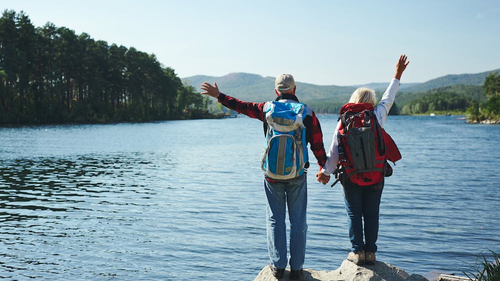 Summer adventure . Couple standing in front of a lake while holding hands and raising the arms up in the air while enjoying the view.<a href='https://www.freepik.com/photos/pension'>Pension photo created by pressfoto - www.freepik.com</a>