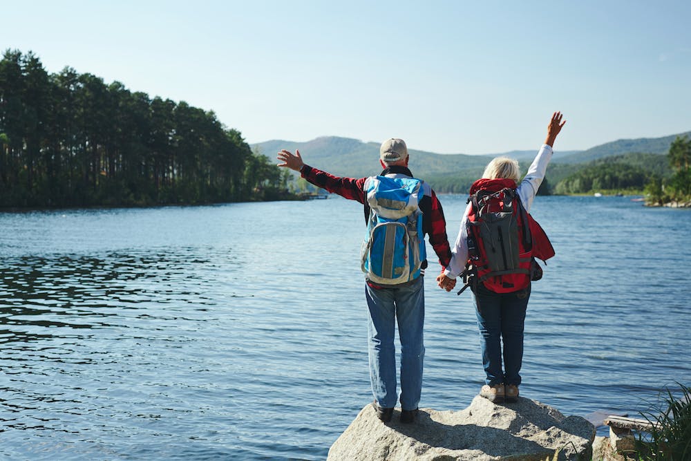 Summer adventure . Couple standing in front of a lake while holding hands and raising the arms up in the air while enjoying the view.<a href='https://www.freepik.com/photos/pension'>Pension photo created by pressfoto - www.freepik.com</a>