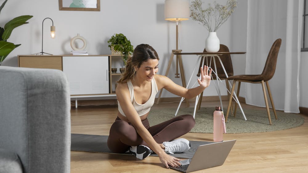 Una monitora de fitness utiliza un ordenador portátil para impartir una clase desde casa- Imagen por <a href="https://www.freepik.com/free-photo/female-fitness-instructor-using-laptop-teach-class-from-home_23674959.htm#query=working%20from%20home&position=28&from_view=search">Freepik</a>