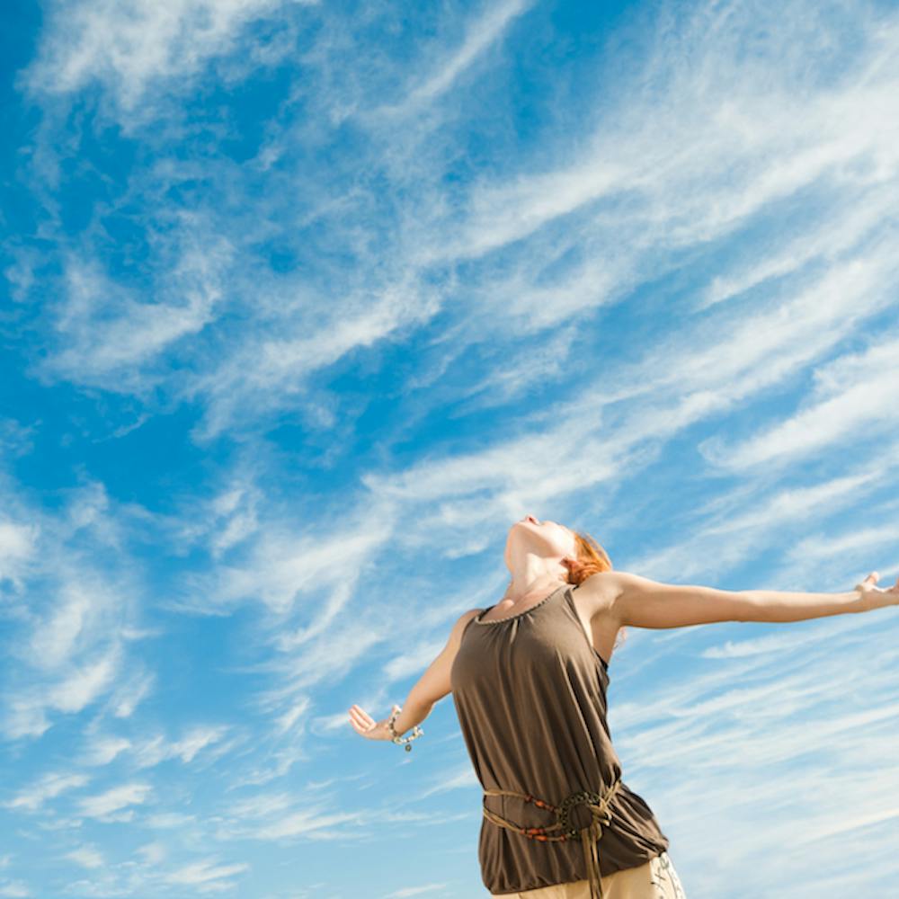 Mujer con brazos abiertos hacia el cielo azul
