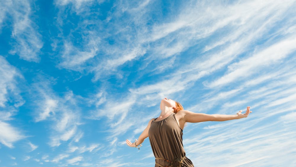Mujer con brazos abiertos hacia el cielo azul