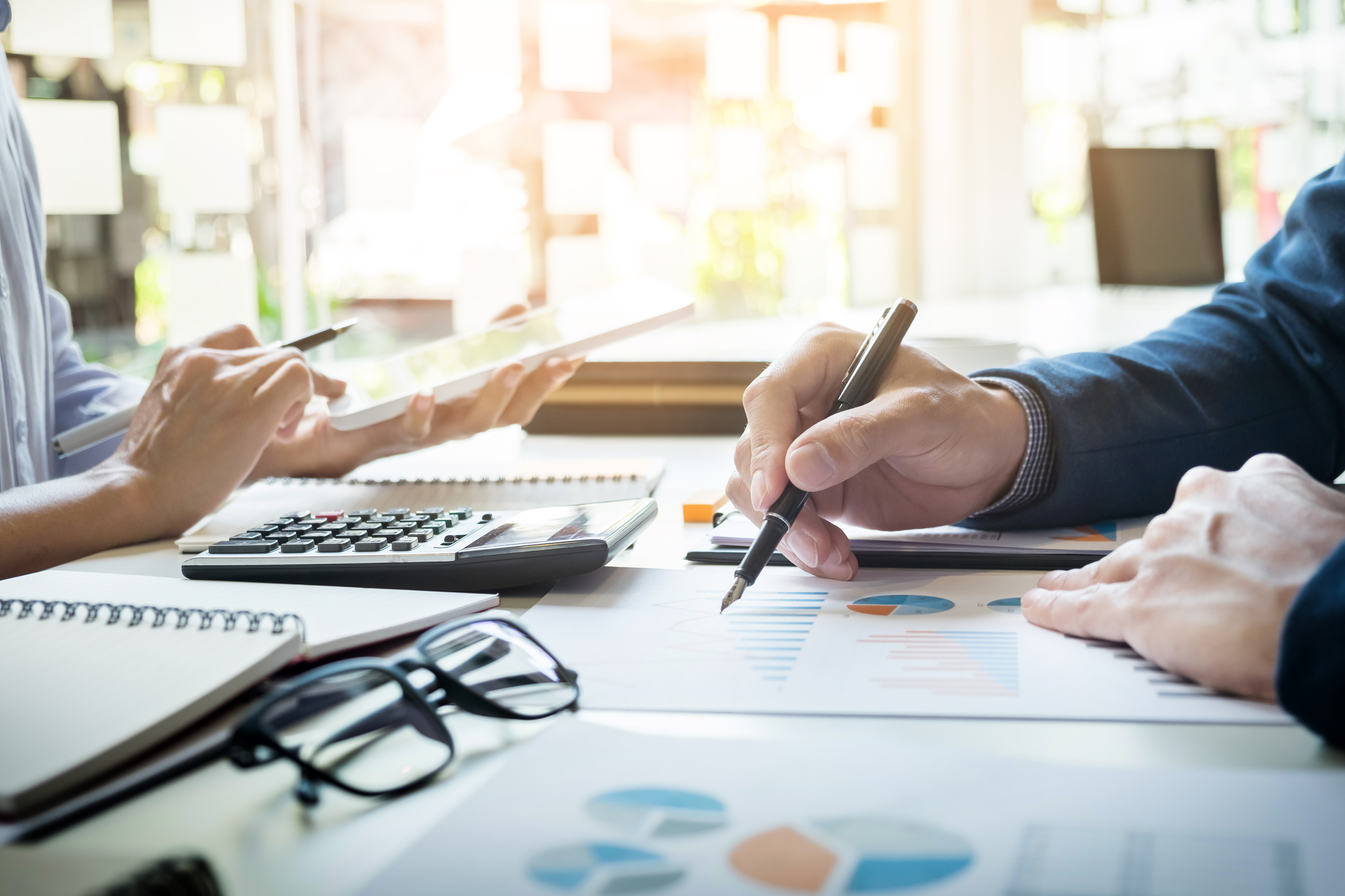 An image of two people, with only their hands visible, who are working above some important looking documents.