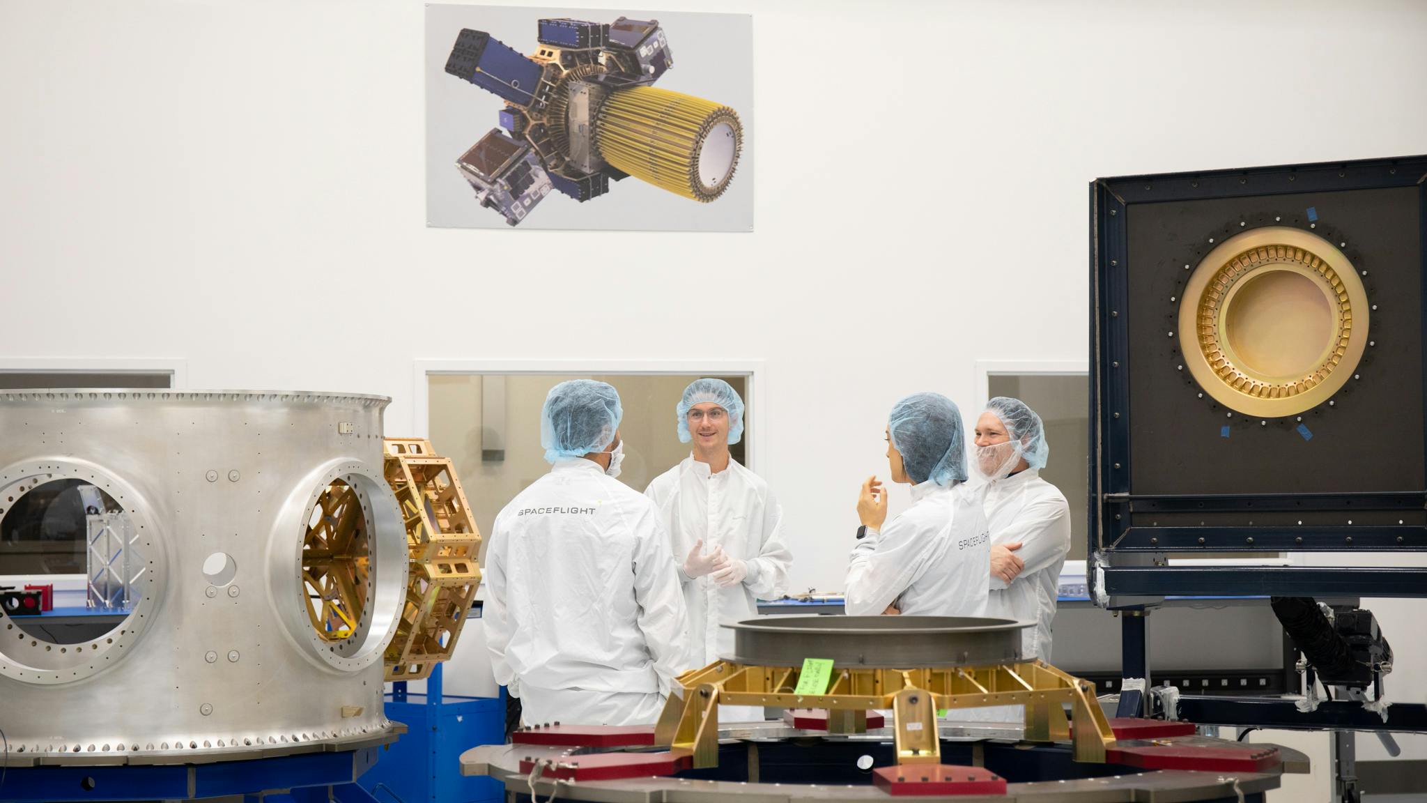 Inside the cleanroom, 4 people in lab coats are in a circle, talking.