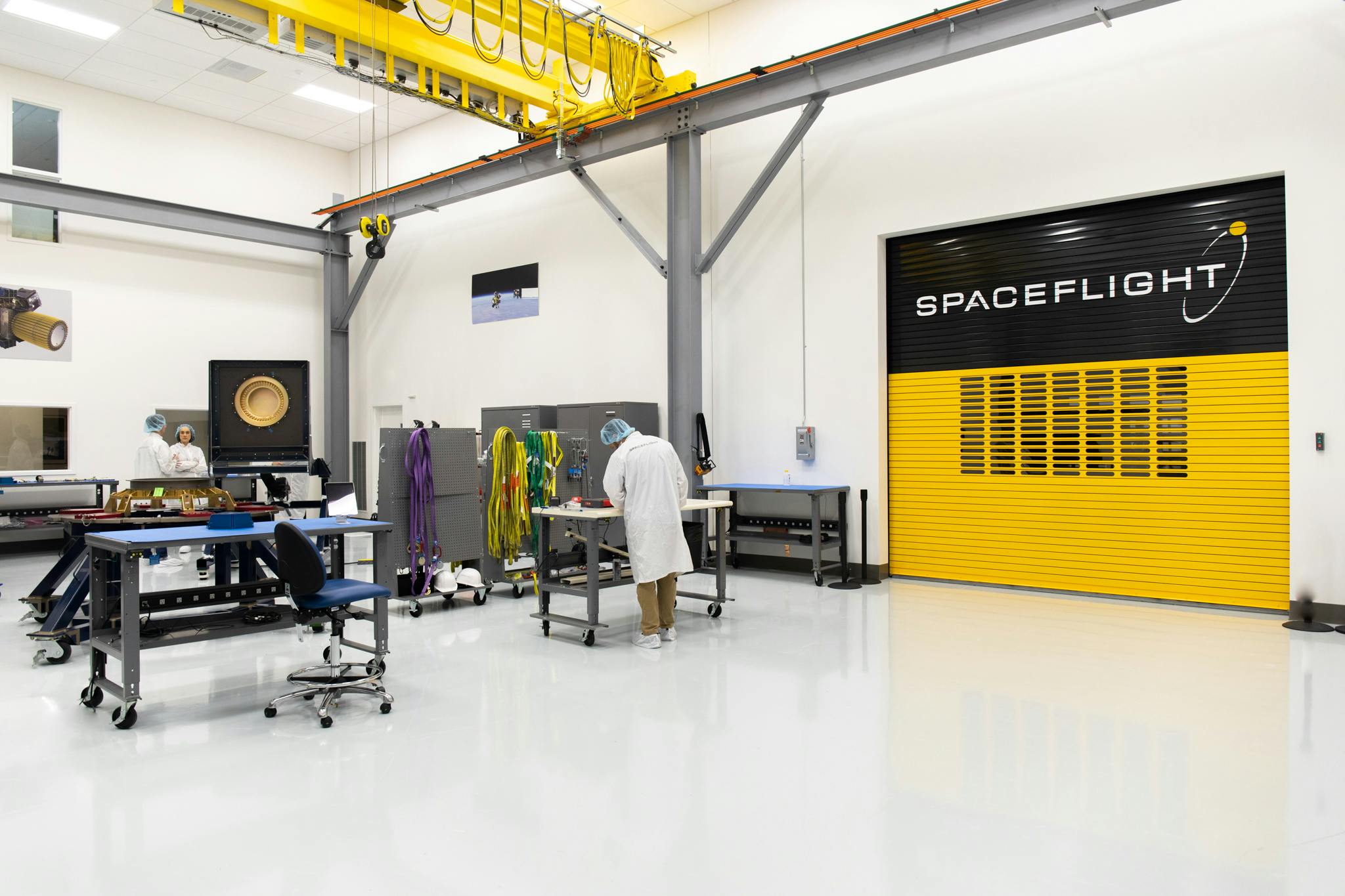 Inside the Spaceflight cleanroom. Large beams for the crane can be seen as well as a black and yellow garage door that has the Spaceflight logo on it. 