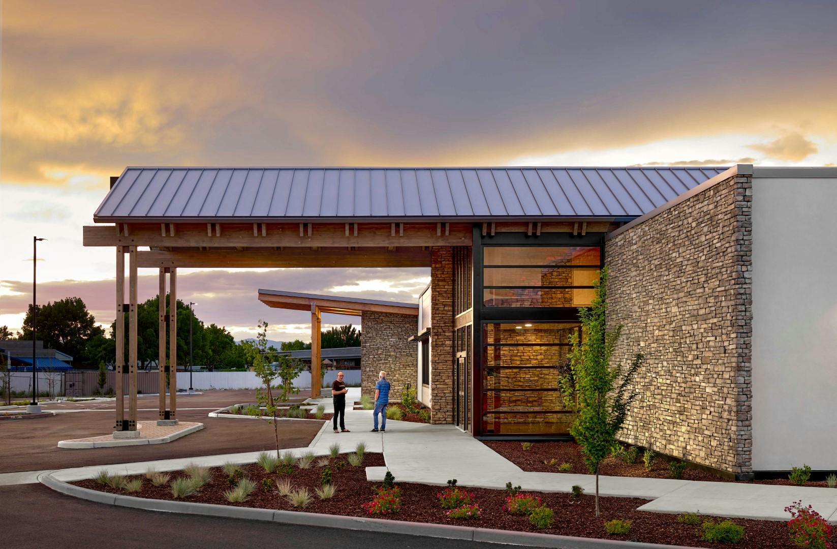 Side exterior of the OOC ambulatory surgery center during sunset. Two people are having a conversation under the canopy for patient drop-off.