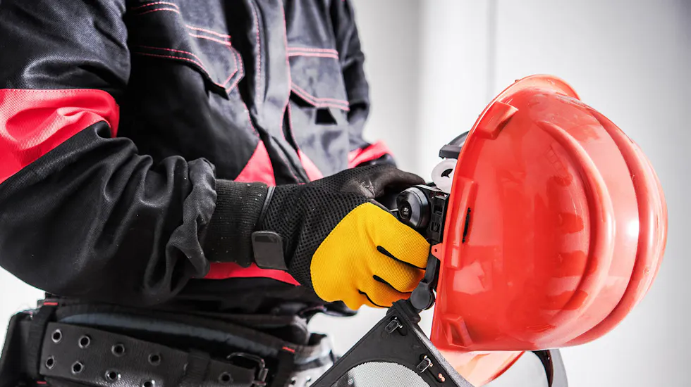 Worker in protective gear putting on gloves next to safety helmet and equipment