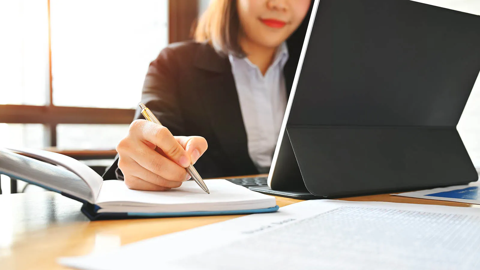 Auditor reviewing compliance documents with a notebook and tablet at a desk