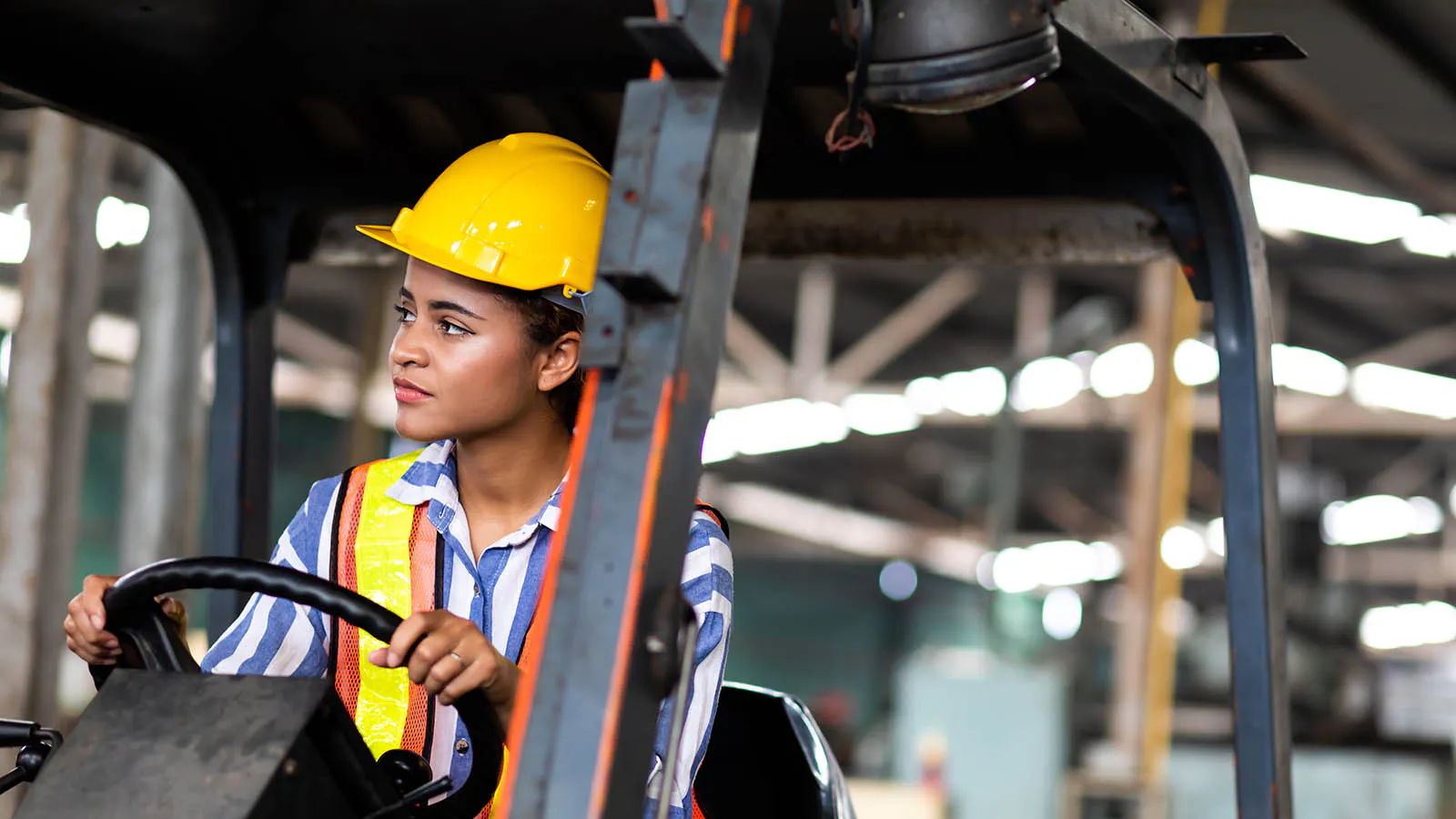 Forklift operator wearing safety goggles and hard hat driving a forklift in a warehouse
