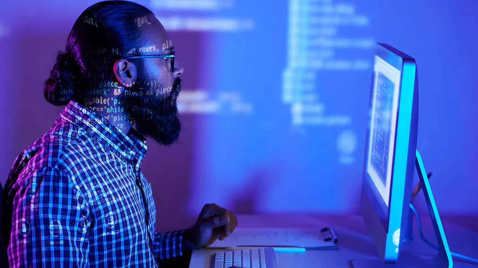 Developer working at a glowing computer screen in a dark office