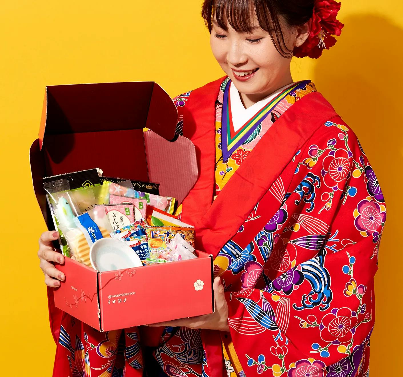 A woman in an Okinawa Bingata Kimono holds Sakuraco's August box.