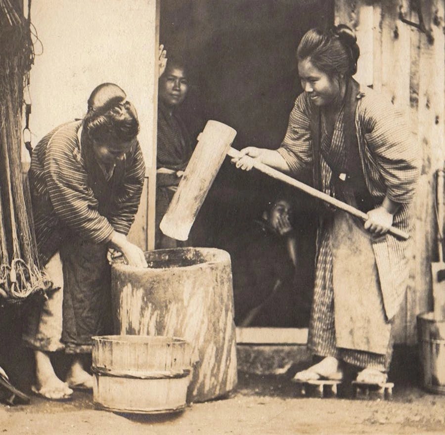 Woman make mochi rice cakes using a traditional mortar and wooden mallet.