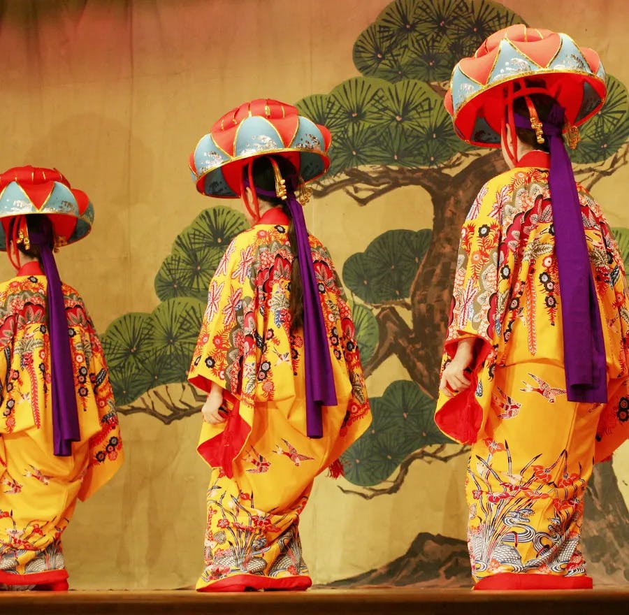 Three eisa dancers are dressed in vibrant and beautiful Okinawan kimonos that are adorned in traditional bingata style.