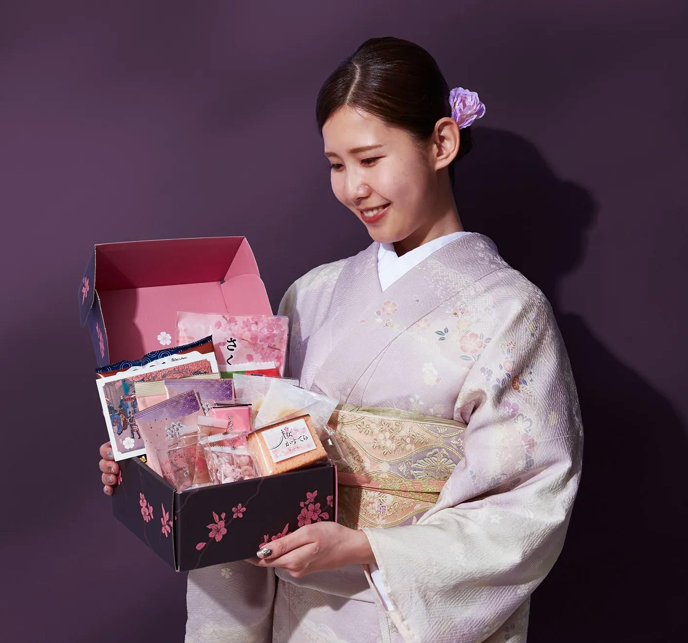 A woman in a kimono stands holding the A Night of Sakura Box