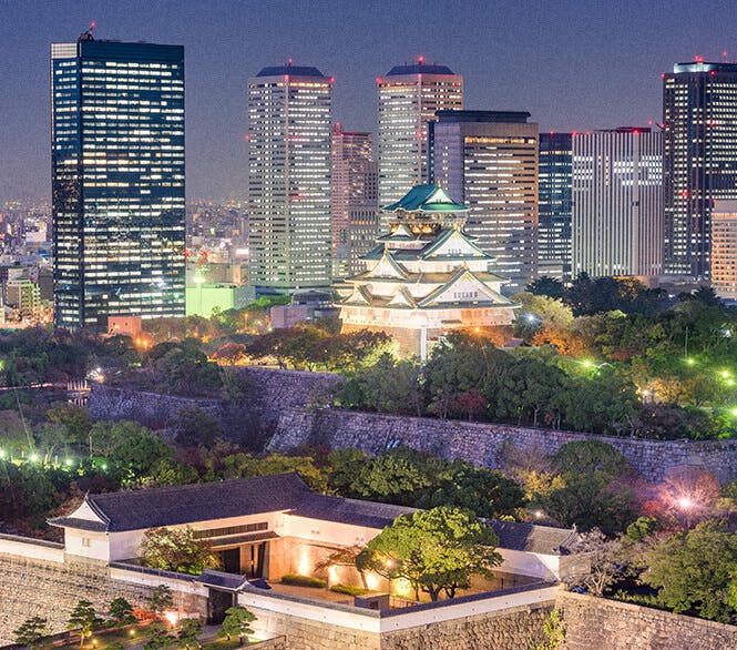 Osaka castle stands glowing at night in front of the Osaka skyline