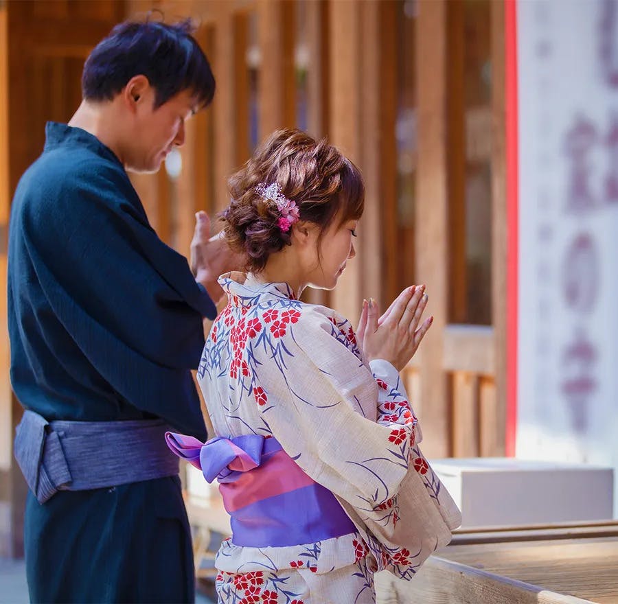 A couple dressed in Japanese yukata pray at a shrine together.