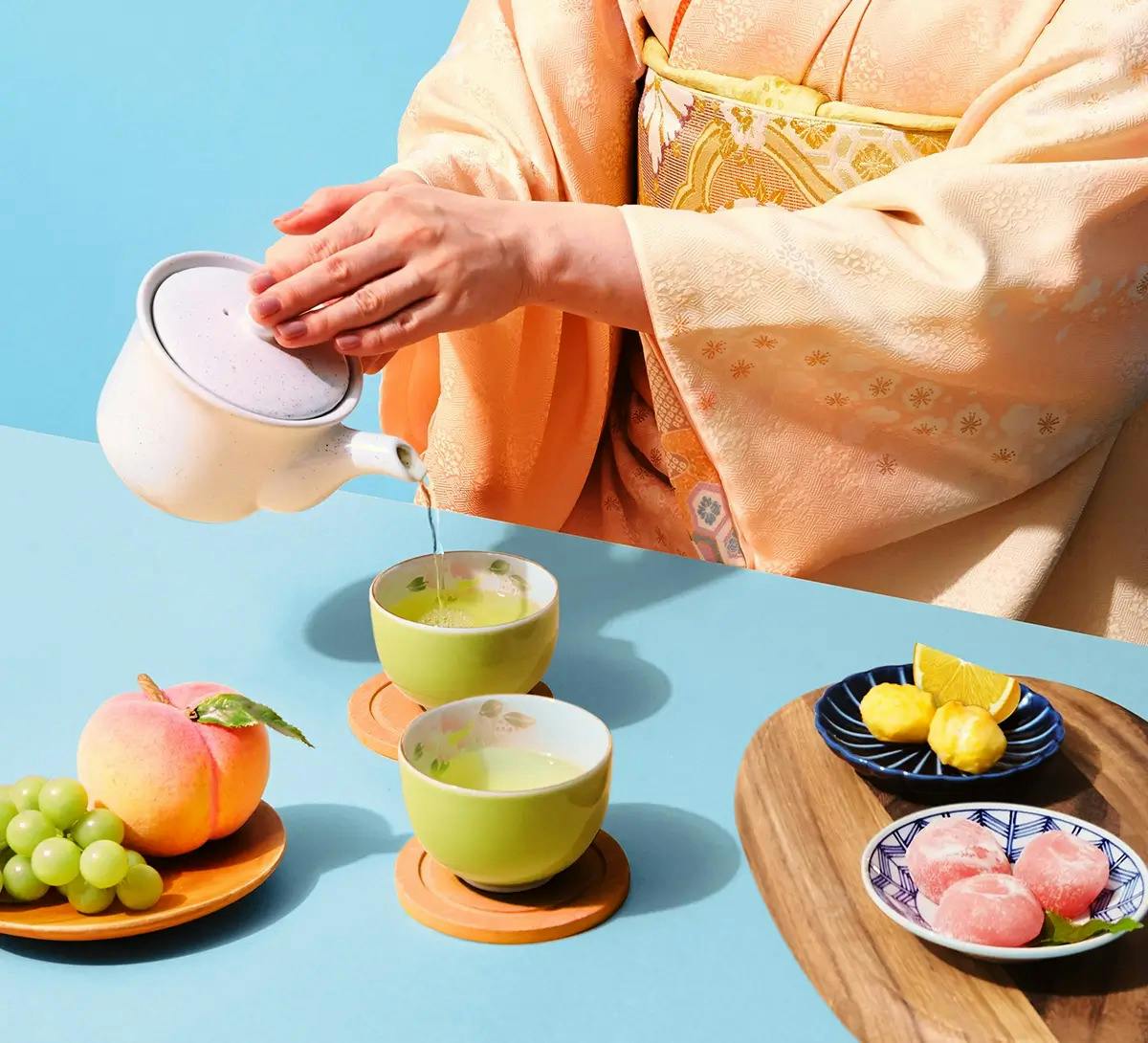 A woman in a peach kimono pours genmaicha surrounded by traditional Japanese snacks.