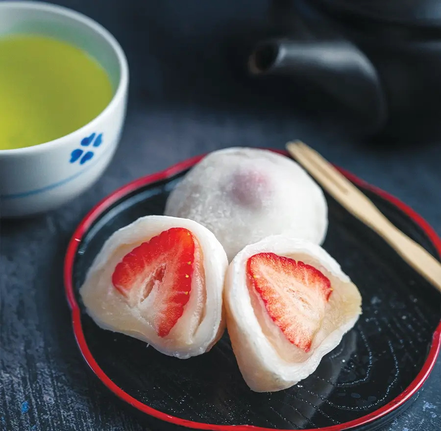 Ichigo Daifuku sits on a black plate next to Japanese green tea.