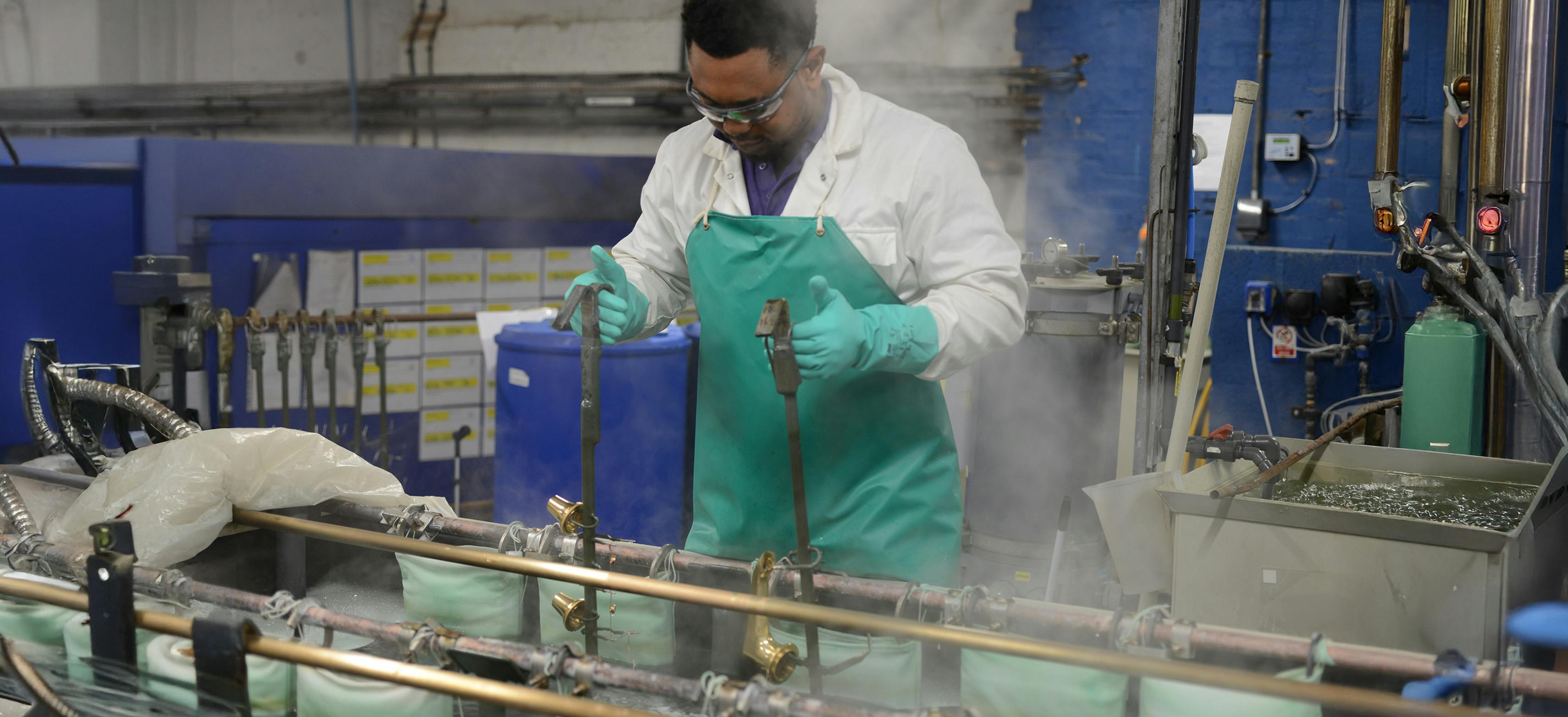 A person at work dipping brassware in the Samuel Heath electroplating shop