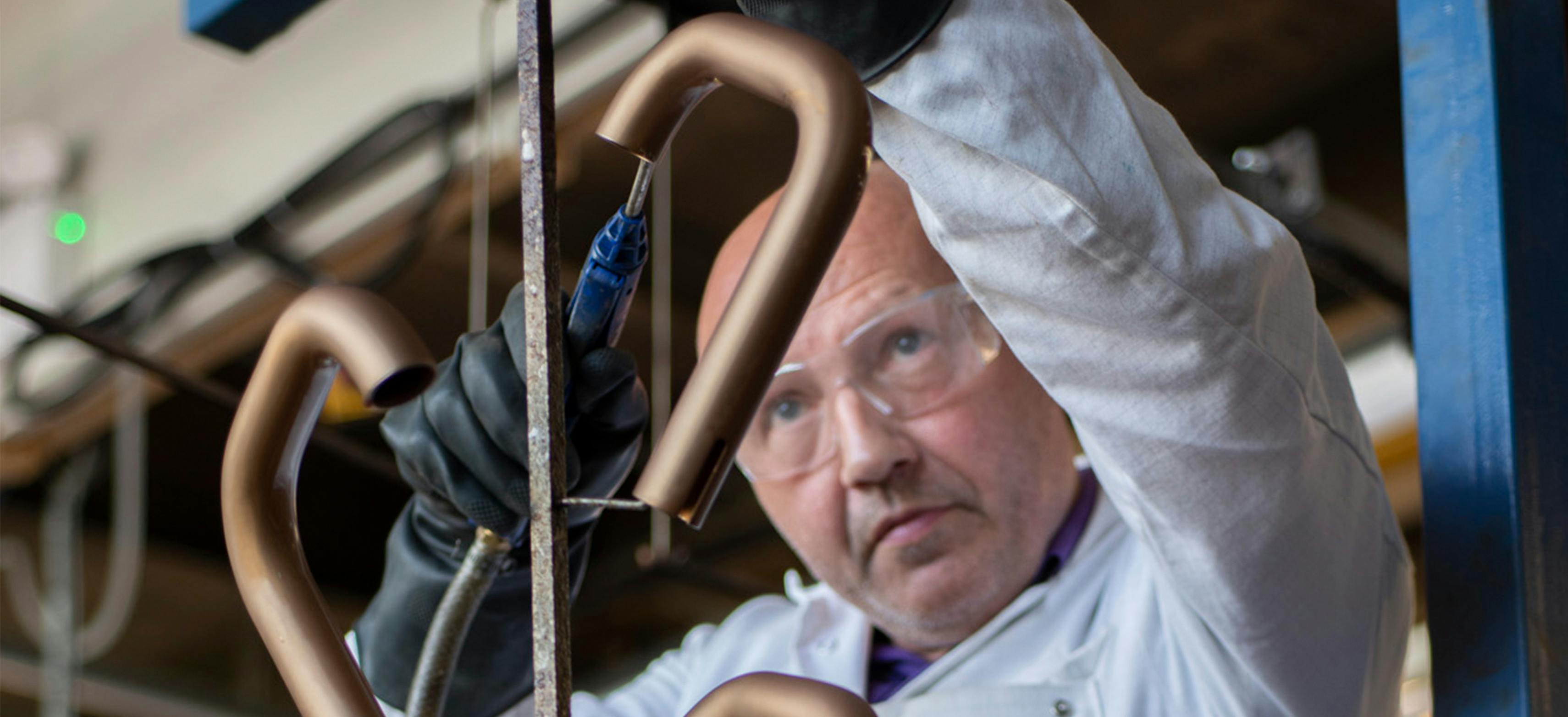 A lacquering technician removing excess air from a metal holder with tap spouts 