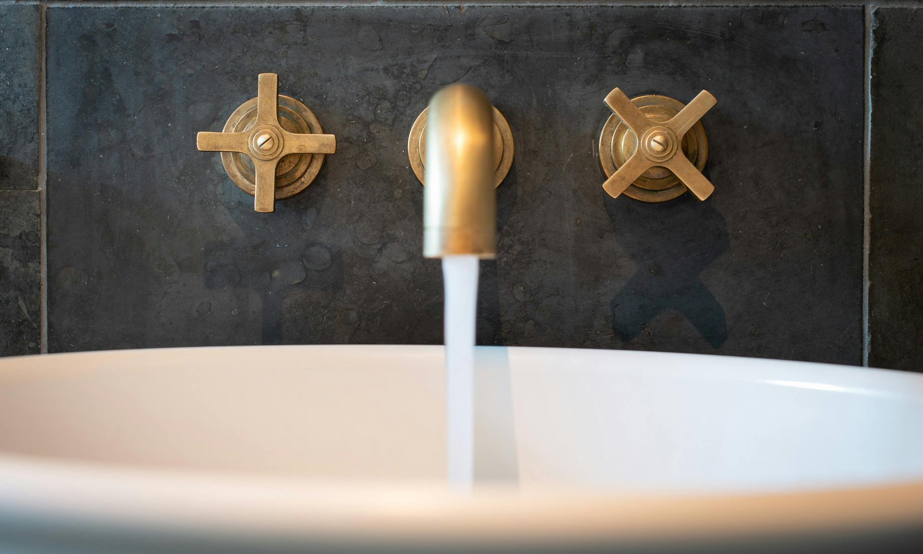 Samuel Heath Bauhaus inspired Landmark Pure wall mounted tap in a natural urban brass finish showing patina.