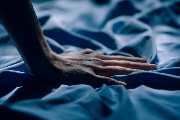 man with hand on bed sheets - how to stay cool while sleeping