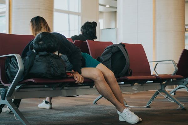 young man suffering from travel insomnia trying to get some sleep at the airport