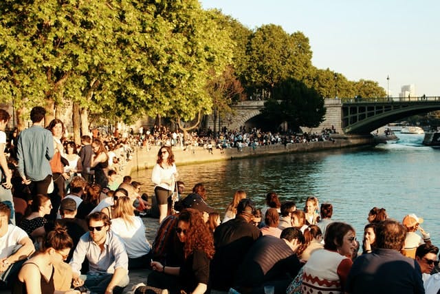 Hundreds of people gather and sit around a sunny riverway during a summers day in Paris, France.