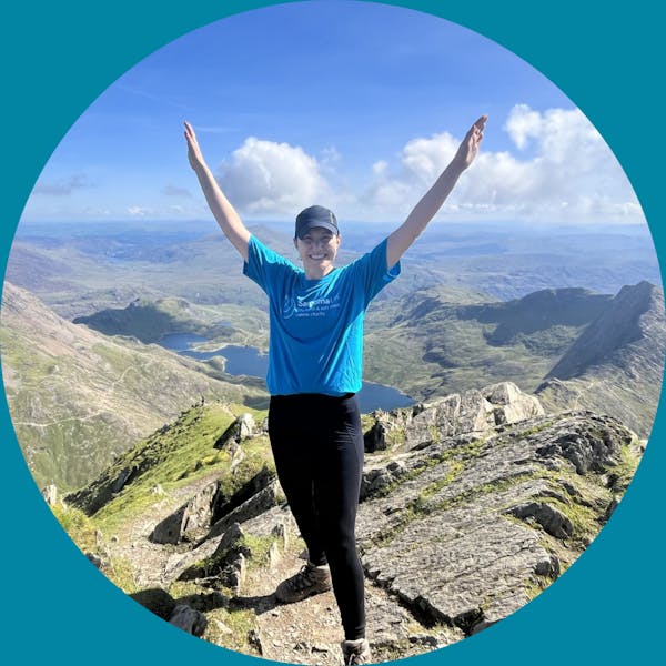 Person atop a mountain with their arms stretched overhead