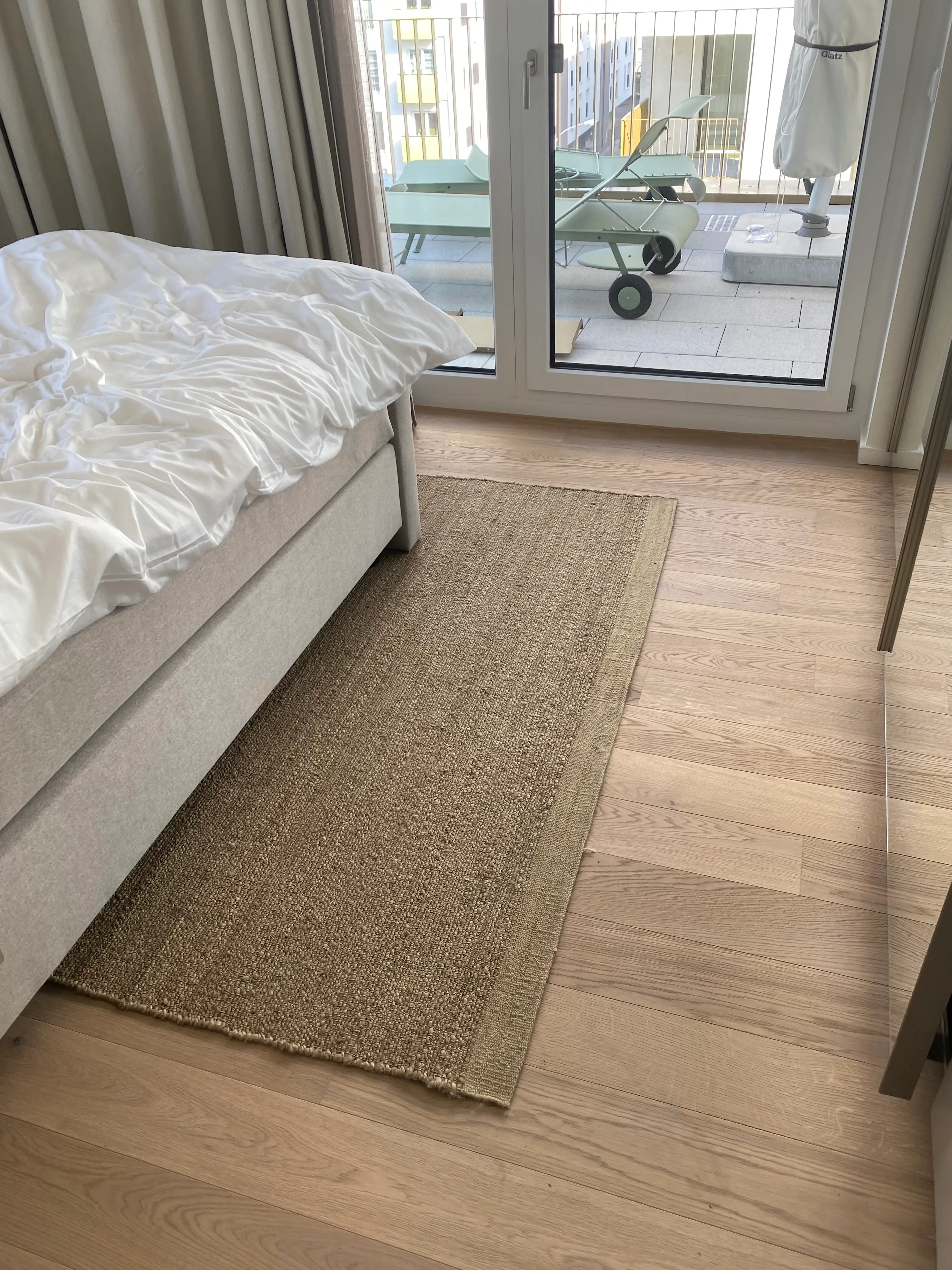 Hochwertiges Bauwerk Parkett im Schlafzimmer mit direktem Zugang zum Balkon, kombiniert mit einem Naturfaserteppich.
