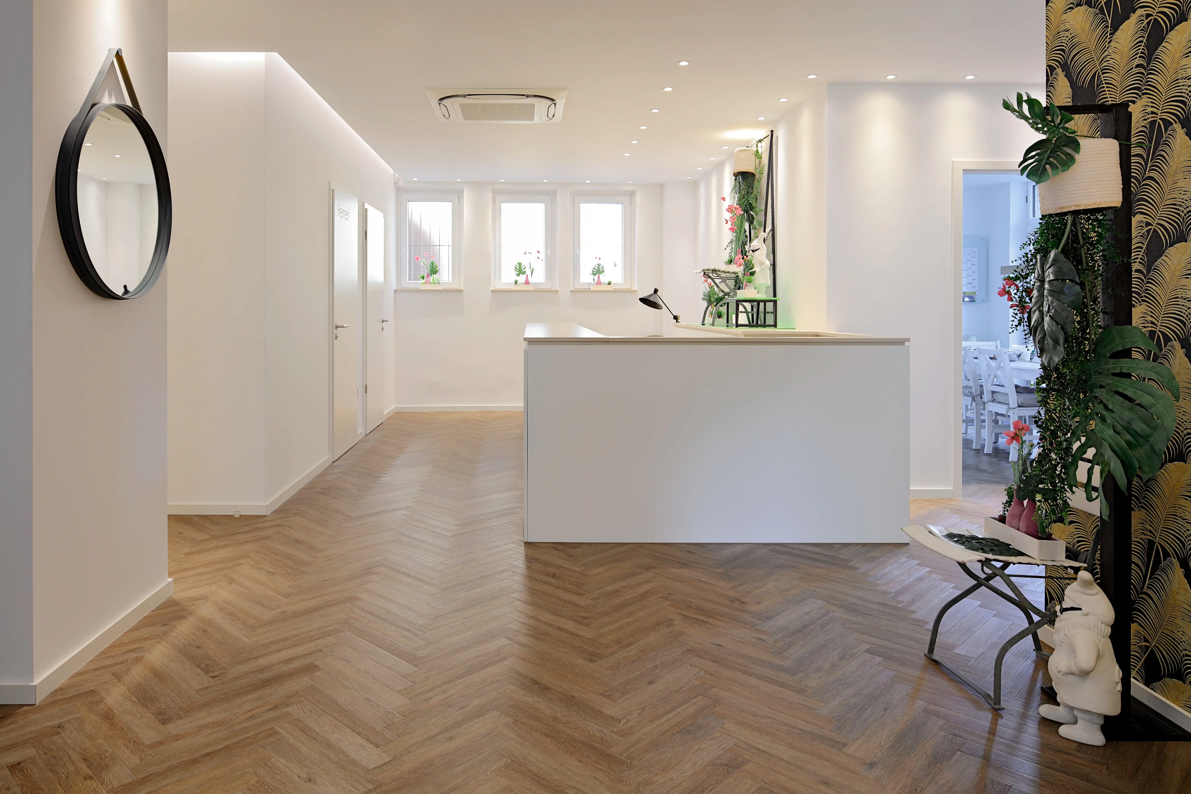 Heller, weitläufiger Flurbereich im Ladengeschäft mit weißen Wänden, einer minimalistischen weißen Theke und durchgehend von Parkett Saussele verlegtem Fischgrät-Vinyl für ein fließendes Raumgefühl.