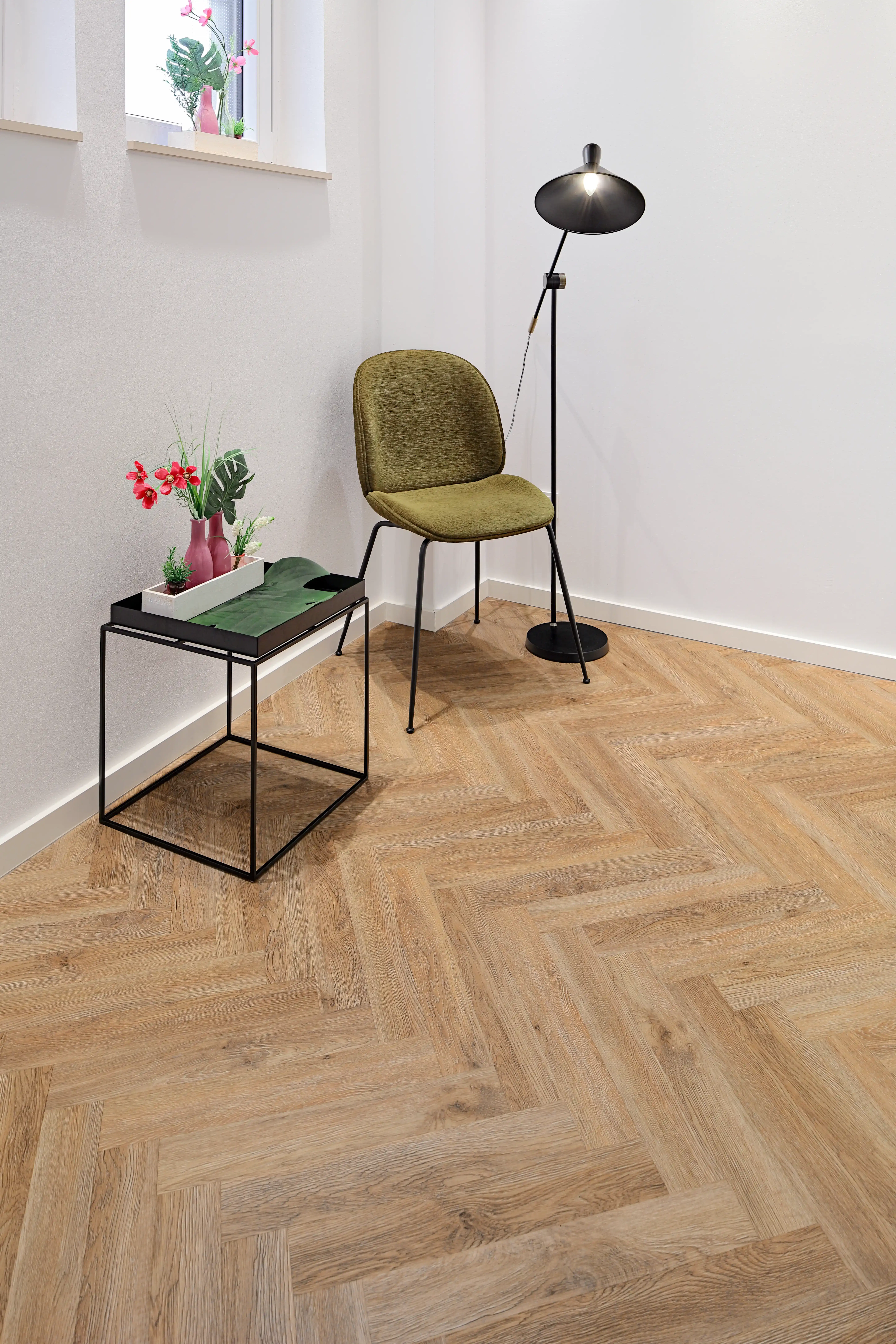 Detailaufnahme der präzisen Verlegung des Fischgrät-Vinyls in einer stilvollen Raumecke mit olivegrünem Design-Stuhl, schwarzer Stehlampe und minimalistischem Beistelltisch.