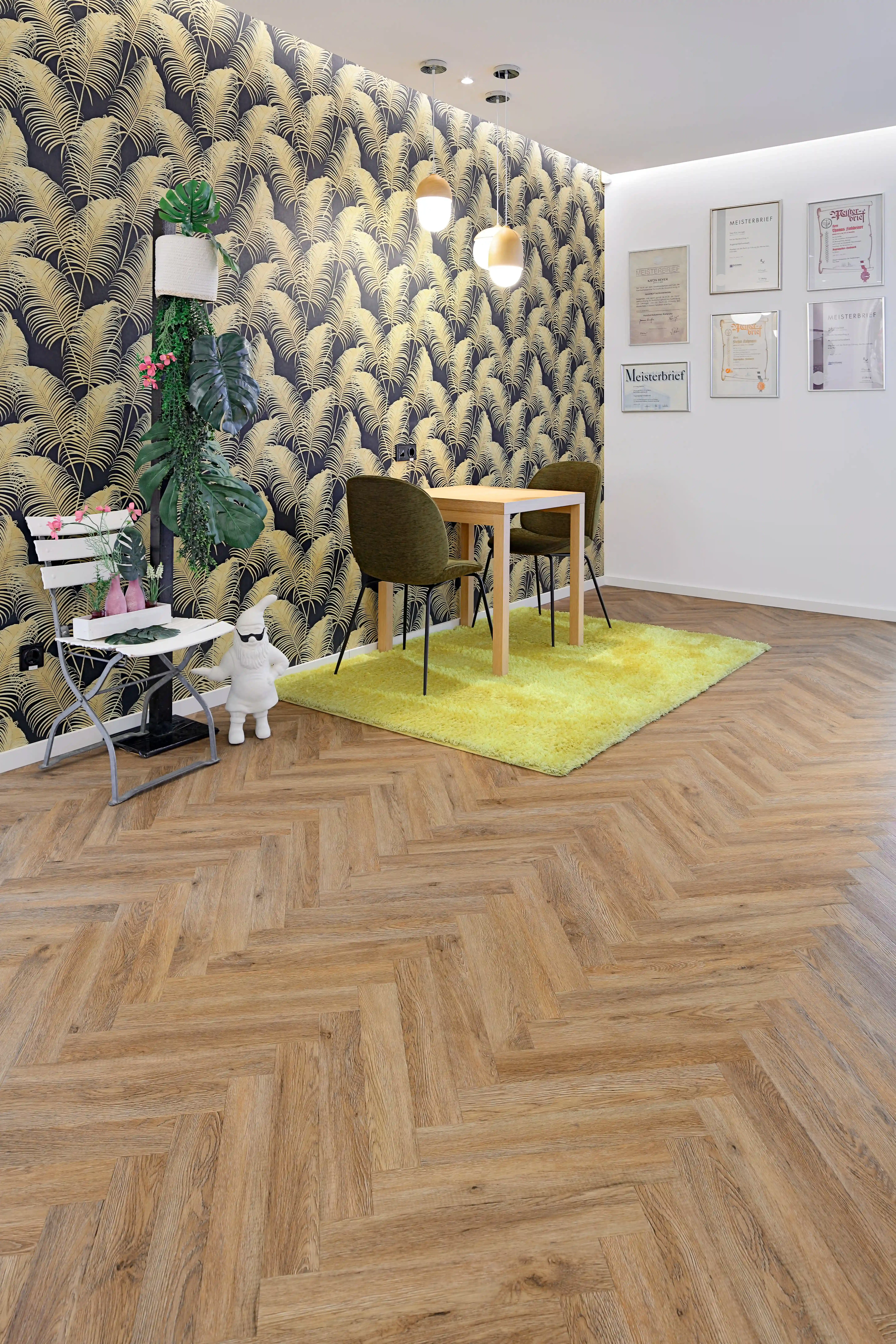 Gemütliche Beratungsecke mit einer dunkel-goldenen Palmenblatt-Tapete, limettengrünem Teppich und Holztisch, perfekt abgerundet durch das präzise Verlegemuster des Fischgrät-Vinyls.