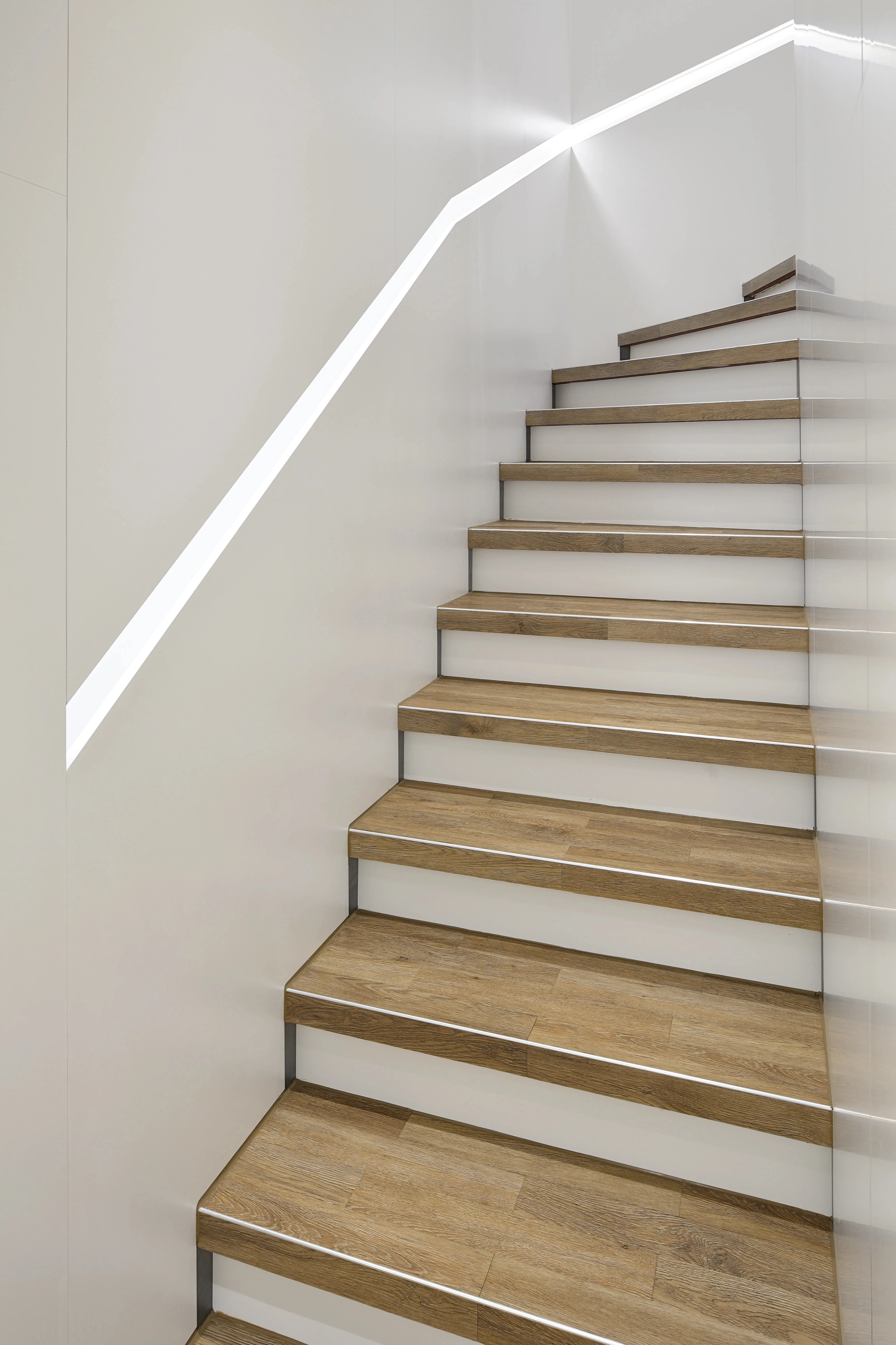 Stilvolle Treppensanierung im Optikerladen Pforzheim: Mit strapazierfähigem Vinyl in Holzoptik verkleidete Stufen, kombiniert mit weißen Setzstufen und einem modernen, integrierten LED-Lichtband an der Wand.